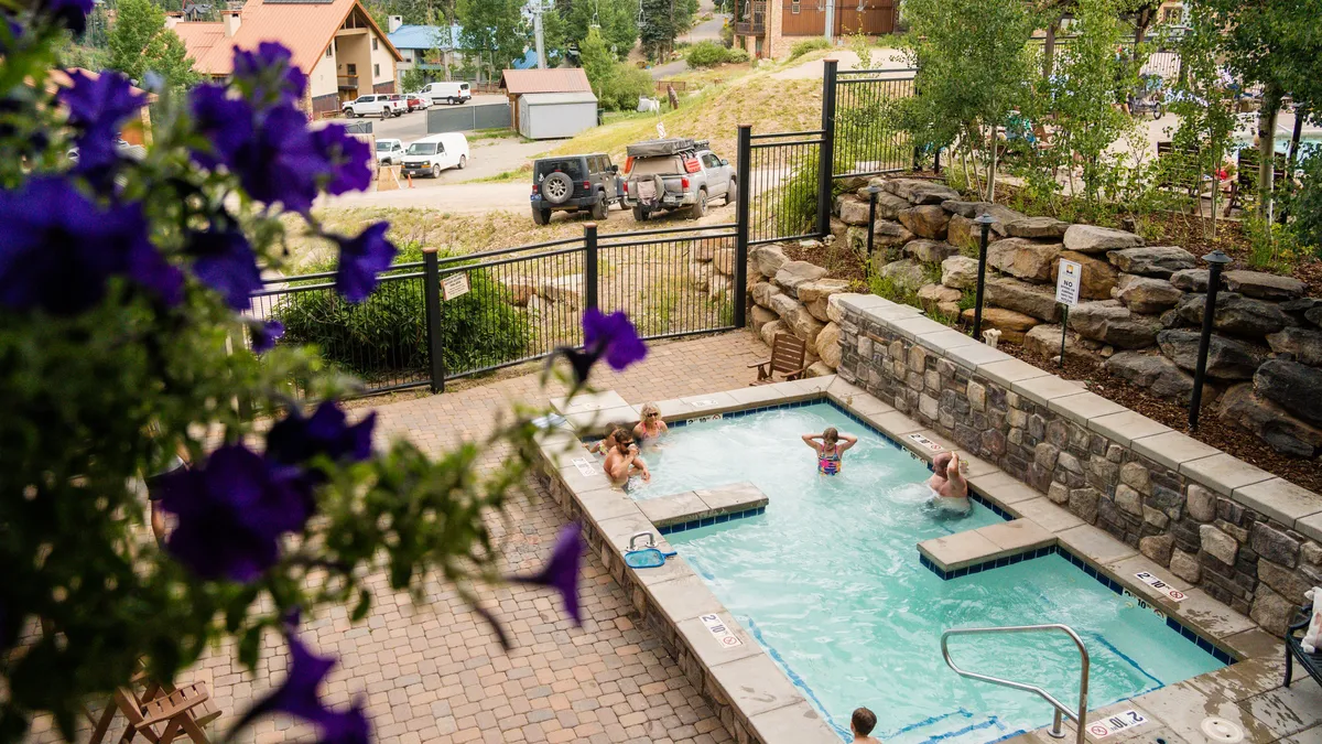 An exterior shot of a sparkling swimming pool surrounded by blooming flowers, a sturdy stone wall, and a comfortable seating area. The image exudes warmth, inviting relaxation and sociability in an outdoor setting perfect for summer gatherings and post-adventure unwinding.