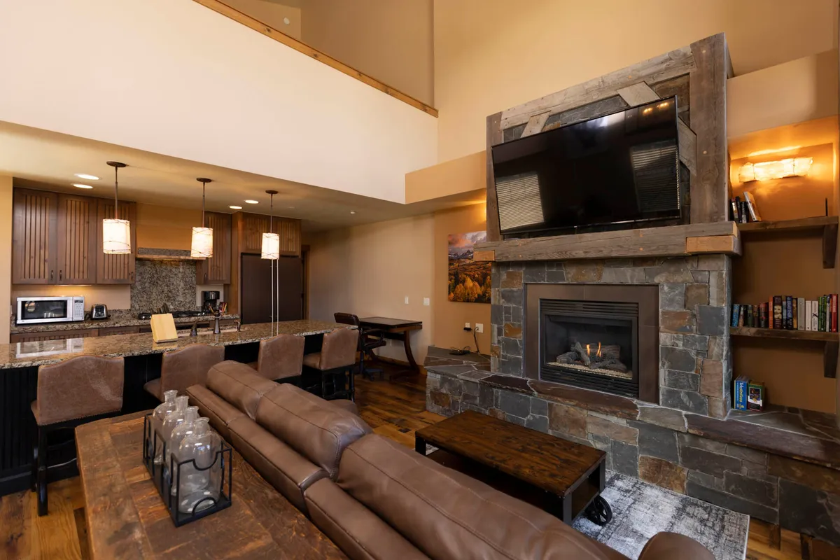 A warm, welcoming interior featuring a sofa, fireplace, kitchen island, and television. The space is designed for relaxation and entertaining after a day on the slopes, blending modern comforts with cozy mountain charm.