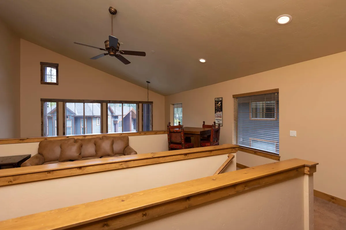 A comfortable living area with a sofa adorned with cushions, wooden railing, dining table with chairs, and large windows that fill the space with natural light. The area is ideal for relaxation, socializing, and offers sleeper sofa options for additional guests.